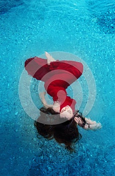 Beautiful young woman in red evening dress elegant floating weightlessly in the water in the pool dark brown curly hair floating