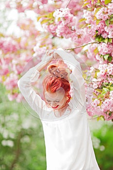 Beautiful young woman with red hair having fun standing in cherry blossom tree