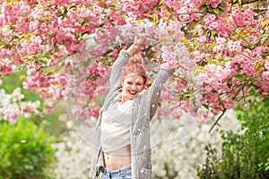 Beautiful young woman with red hair having fun standing in cherry blossom tree