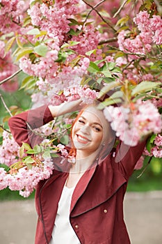 Beautiful young woman with red hair having fun standing in cherry blossom tree