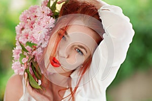 Beautiful young woman with red hair having fun standing in the garden with cherry blossom branch