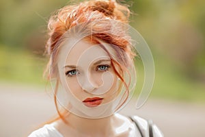 Beautiful young woman with red hair, outside in a park in the sunlight, looking into the camera