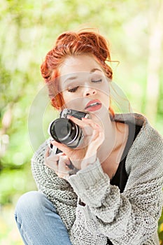 Beautiful young woman with red hair sitting in the garden taking pictures with camera