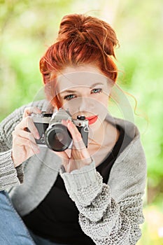 Beautiful young woman with red hair sitting in the garden taking pictures with camera