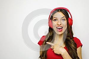 Beautiful young woman with red headphones listening to music smiling and pointing copy space on a white background in a red t-shir