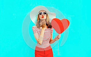 Beautiful young woman with red heart shaped balloons sending sweet air kiss on colorful blue