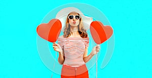 Beautiful young woman with red heart shaped balloons sending sweet air kiss on colorful blue