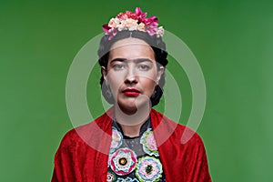 Beautiful young woman with red make up looking like Frida Kahlo. Over green background photo