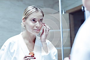 Beautiful young woman with red nails taking care of her skin on face