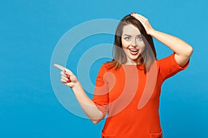 Beautiful young woman in red orange dress standing posing pointing hands fingers on workspace isolated over trendy blue