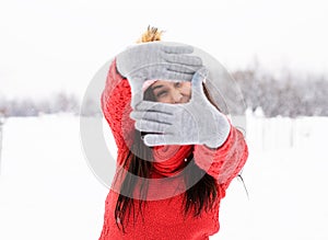 Beautiful young woman in red sweater making frame sign with her hands outdoors in snowy day