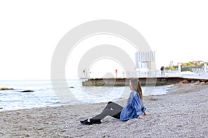 Beautiful young woman relaxes sitting on beach and enjoys view o