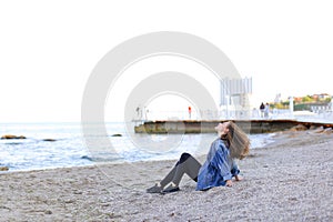 Beautiful young woman relaxes sitting on beach and enjoys view o