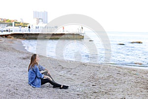 Beautiful young woman relaxes sitting on beach and enjoys view o