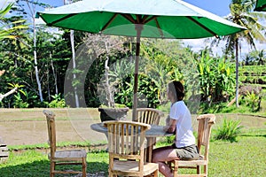 A beautiful young woman relaxes on a warung`s terrace close to typical rice paddies after a trek under the sun in Ubud. photo