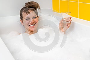 Beautiful young woman is relaxing in bath with foam