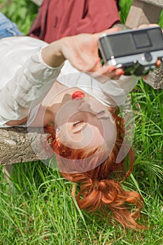 Beautiful young woman relaxing with camera in her hand on garden bench in green grass