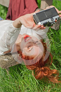 Beautiful young woman relaxing with camera in her hand on garden bench in green grass