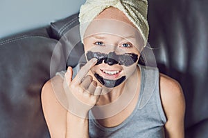 Beautiful young woman relaxing with face mask at home. Happy joyful woman applying black mask on face