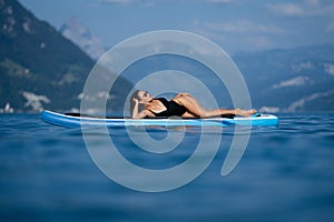 Beautiful young woman relaxing on paddle board in the summer lake or sea water. Summer resort. Sexy sensual fit woman