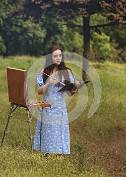 Beautiful young woman is relaxing while painting an art canvas outdoors in the park at rain