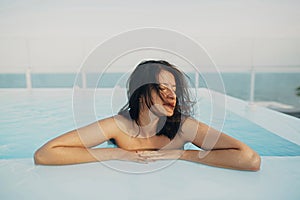 Beautiful young woman relaxing in pool, enjoying warm sunlight and wind. Brunette girl on summer vacation in luxury resort,