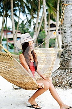 Beautiful young woman relaxing on rattan hammock on the white sand beach during travel vacation