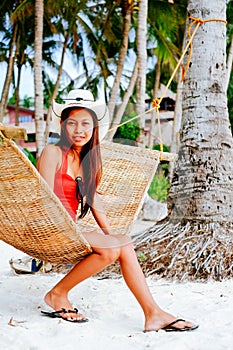 Beautiful young woman relaxing on rattan hammock on the white sand beach during travel vacation