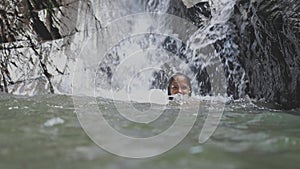 Beautiful young woman relaxing swimming under tropical waterfall. slow motion. 3840x2160