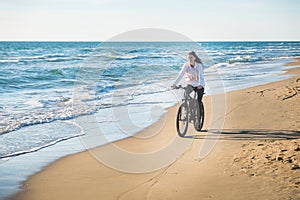 Beautiful young woman rides a Bicycle along the sea on a sandy beach.