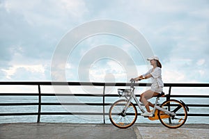 Beautiful young woman riding bicycle along embankment. Space for text