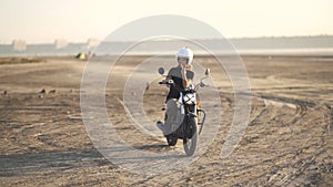 beautiful young woman riding an old cafe racer motorcycle on desert at sunset or sunrise. Female biker. Slow motion