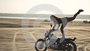 beautiful young woman riding an old cafe racer motorcycle and doing a trick. in the desert at sunset or sunrise. Female biker