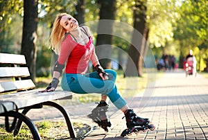 Beautiful young woman in roller skates sitting on park bench