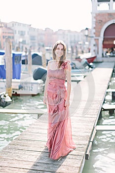 Beautiful young woman in rose dress standing on the background of Venice canal, buildings and gondola. Italy, Europe.