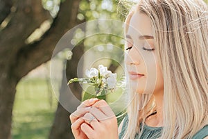 Beautiful young woman`s face close-up woman holding a branch of a flowering tree in her hands and sniffing flowers with her eyes