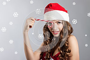 Beautiful young woman in a Santa Claus hat. Christmas portrait of a girl with a licorice candy