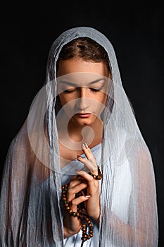 Beautiful young woman with a scarf on her head, and a rosary in her hands, humble look, believing woman