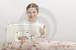 Beautiful young woman sews a curtain on a sewing machine and shows her thumb. The concept of successful business development