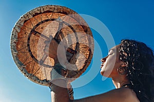 Beautiful young woman with shaman drum outdoors and playing ethnical music