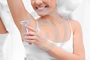 Beautiful young woman shaving armpit at home