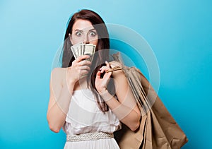 Beautiful young woman with shopping bags and money standing in f