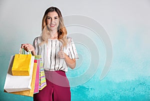 Beautiful young woman with shopping bags showing thumb-up on color background