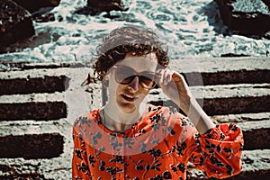 Beautiful young woman with short curly hair looking at camera. Female retro sun protection sunglasses. Enjoy summer vacation