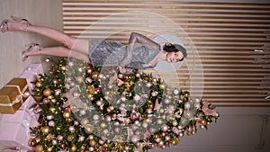 beautiful young woman in a short dress stands at the Christmas tree in the studio. a model poses for the camera at a