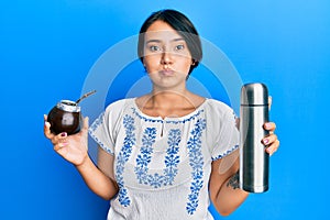 Beautiful young woman with short hair drinking mate infusion puffing cheeks with funny face