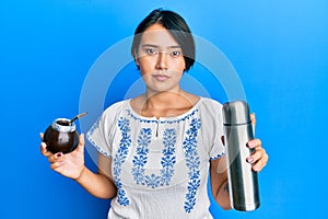 Beautiful young woman with short hair drinking mate infusion relaxed with serious expression on face