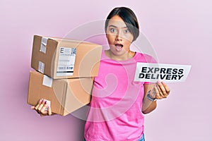 Beautiful young woman with short hair holding delivery box with express delivery text afraid and shocked with surprise and amazed