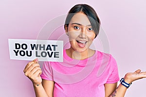 Beautiful young woman with short hair holding paper with do what you love text celebrating achievement with happy smile and winner