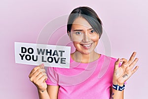 Beautiful young woman with short hair holding paper with do what you love text doing ok sign with fingers, smiling friendly